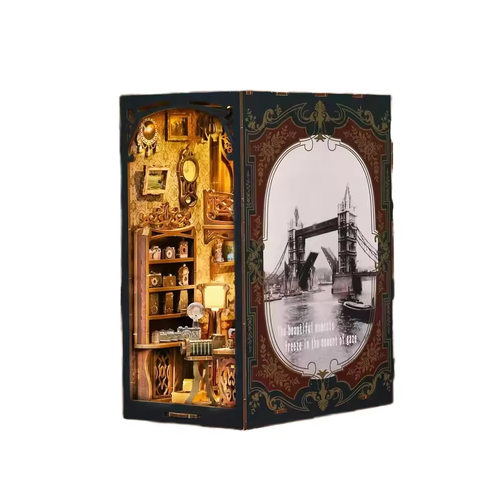 Maquette serre-livres (Book Nook) 'Film Darkroom' présentant un intérieur de studio photo rétro avec étagères d'appareils photo miniatures et une façade latérale illustrée du Tower Bridge de Londres.