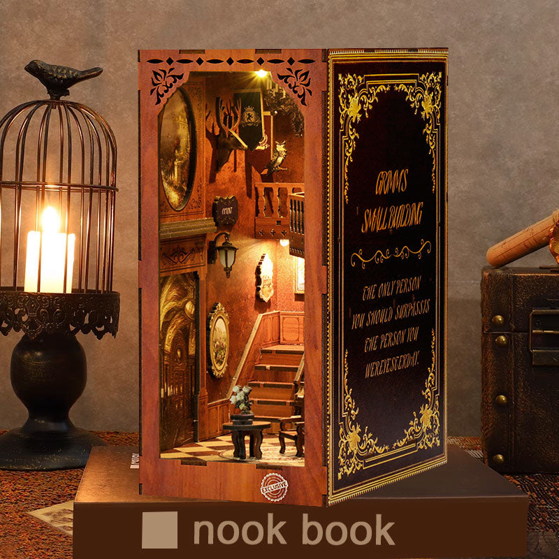 Un Book Nook en bois posé sur un livre socle, mis en scène à côté d'une cage à oiseaux contenant une bougie allumée. La scène miniature intérieure représente un hall de manoir chaleureux avec un escalier et des détails vintage, créant une ambiance de décoration d'intérieur cosy et mystérieuse.