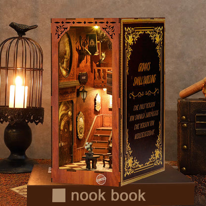Un Book Nook en bois posé sur un livre socle, mis en scène à côté d'une cage à oiseaux contenant une bougie allumée. La scène miniature intérieure représente un hall de manoir chaleureux avec un escalier et des détails vintage, créant une ambiance de décoration d'intérieur cosy et mystérieuse.