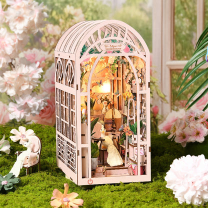 Vue détaillée d'un serre-livres miniature en bois en forme de serre fleurie rose, avec éclairage intérieur chaleureux, plantes miniatures et décor floral romantique.