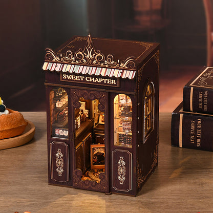 Maquette DIY Book Nook Sweet Chapter avec porte ouverte révélant une pâtisserie miniature détaillée. Décoration de bibliothèque avec éclairage LED et étagères de gâteaux miniatures.