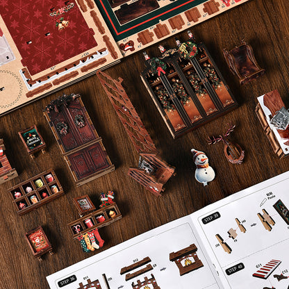 Serre-livres miniature DIY Book Nook 'Christmas Shop' en bois illuminé. La scène montre une boutique de Noël magique avec un grand sapin enneigé, un balcon décoré d'un bonhomme de neige, des cadeaux emballés et des éclairages LED chaleureux aux tons rouges et verts festifs.