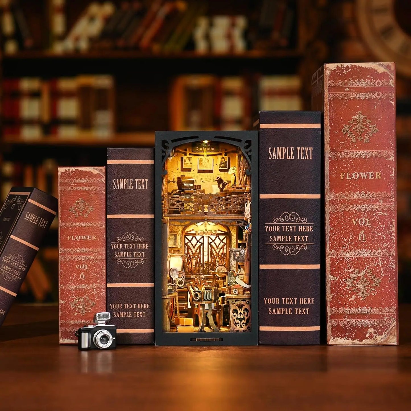Serre-livres miniature DIY (Book Nook) inséré dans une bibliothèque entre des livres anciens, représentant un studio de photographie rétro détaillé avec un éclairage LED chaleureux et un appareil photo miniature au premier plan.