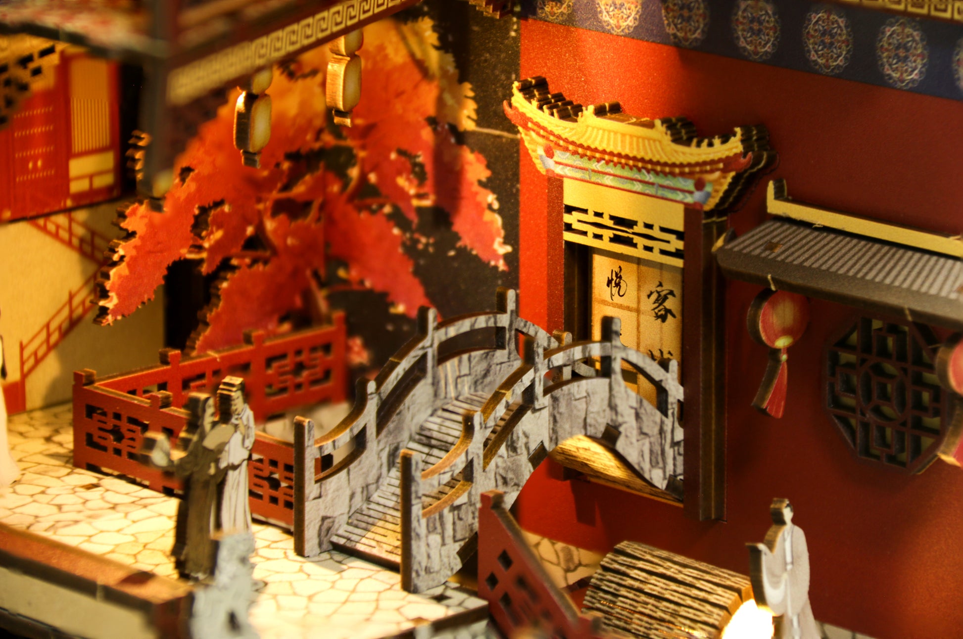 Détail d'un Book Nook DIY en bois : petit pont traditionnel, personnages miniatures et décor de la Chine ancienne avec éclairage tamisé.
