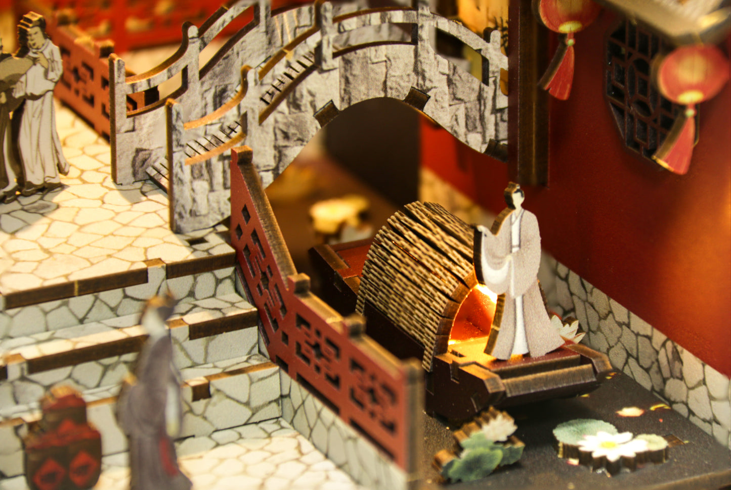 Gros plan d'un kit miniature Book Nook : barque traditionnelle sur une rivière avec nénuphars, pont en pierre et figurines chinoises en bois découpé au laser.