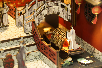 Gros plan d'un kit miniature Book Nook : barque traditionnelle sur une rivière avec nénuphars, pont en pierre et figurines chinoises en bois découpé au laser.