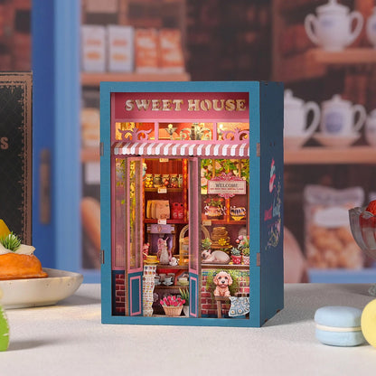 Kit DIY Book Nook Sweet House : maquette de pâtisserie miniature en bois avec éclairage LED. Scène de boutique romantique avec fleurs, gâteaux miniatures, et décors de café cosy pour étagère à livres.