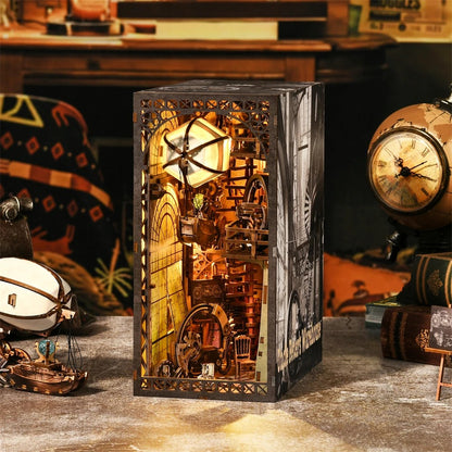 Maquette Book Nook style industriel et steampunk "Uncle Brian's Warehouse" avec éclairage LED chaleureux. Le design présente une structure en bois sombre avec des engrenages complexes, une montgolfière suspendue, des escaliers miniatures et des détails mécaniques. La scène est intégrée dans un serre-livres décoratif pour bibliothèque, créant un effet de profondeur et de perspective.