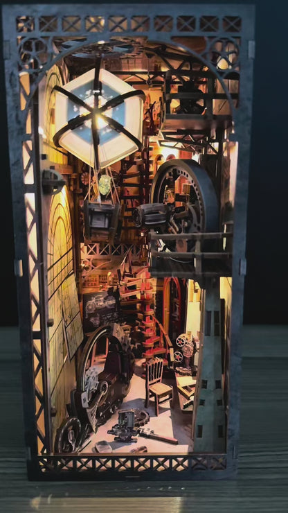 Vidéo de présentation d'une maquette Book Nook animée au style steampunk intitulée "Uncle Brian's Warehouse". La caméra explore l'intérieur détaillé en bois, révélant une montgolfière qui oscille doucement, des engrenages en mouvement et une grande roue mécanique. L'éclairage LED chaleureux met en relief les escaliers en colimaçon, un projecteur de cinéma miniature et une moto rétro. Cette décoration de bibliothèque crée une ambiance industrielle vintage fascinante.