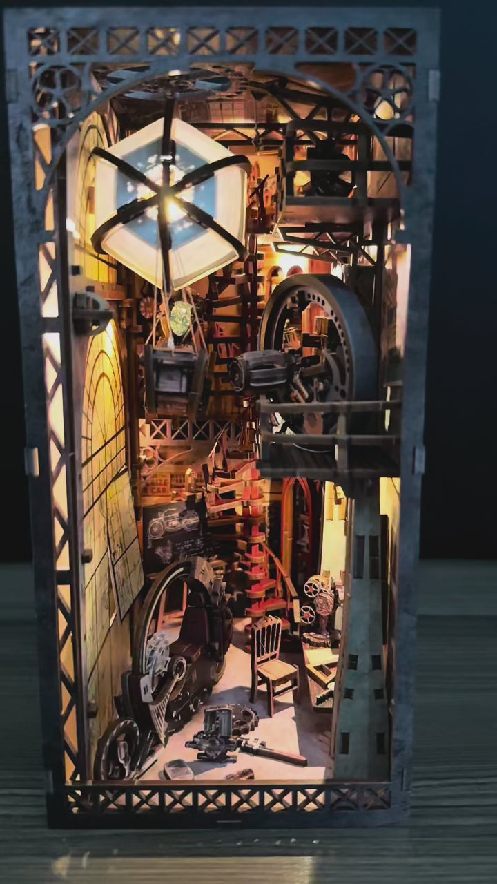 Vidéo de présentation d'une maquette Book Nook animée au style steampunk intitulée "Uncle Brian's Warehouse". La caméra explore l'intérieur détaillé en bois, révélant une montgolfière qui oscille doucement, des engrenages en mouvement et une grande roue mécanique. L'éclairage LED chaleureux met en relief les escaliers en colimaçon, un projecteur de cinéma miniature et une moto rétro. Cette décoration de bibliothèque crée une ambiance industrielle vintage fascinante.